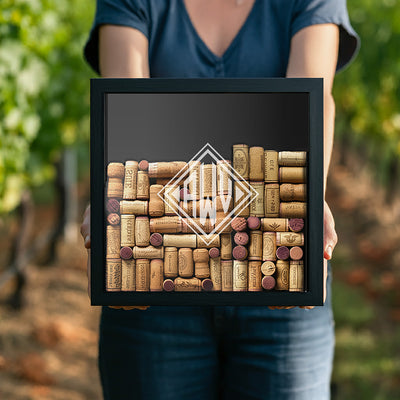 Person holding framed display filled with wine corks and a monogram in the center.