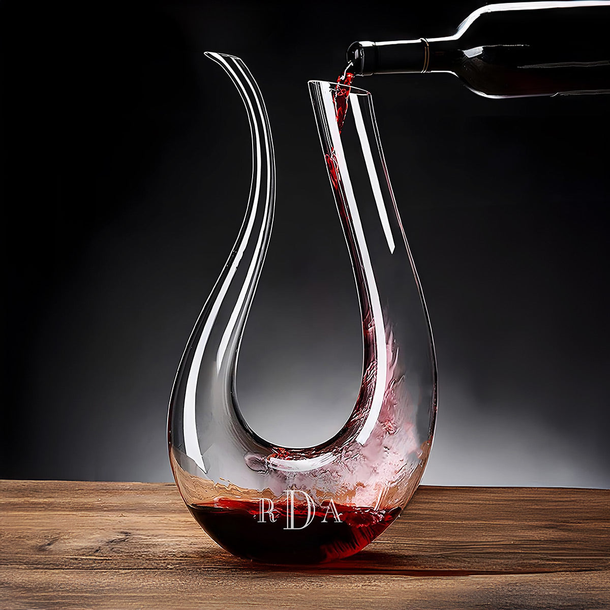 Red wine being poured from a bottle into a curved glass decanter on a wooden table.