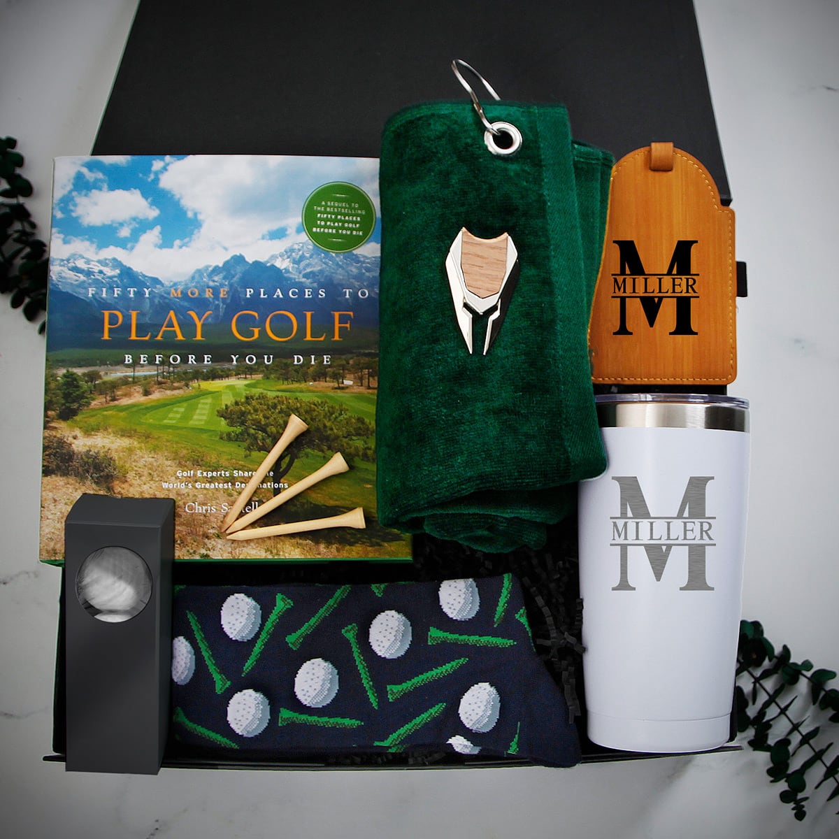Golf-themed gift box with golf book, tees, green towel, wooden tag, patterned socks, and white “M Miller” tumbler.