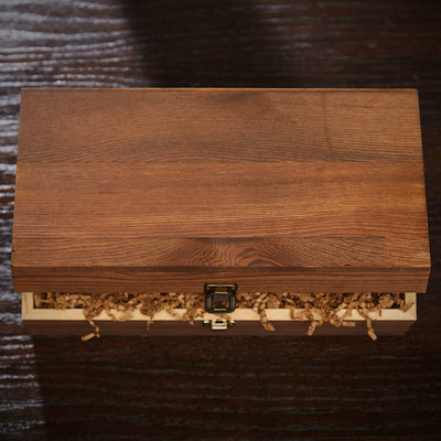 Wooden box with metal latch, slightly open, showing crinkle paper filler inside on a dark surface.