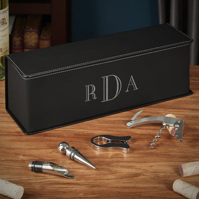 Black leather case with monogram “RDA” on a wooden table beside wine accessories and corks.