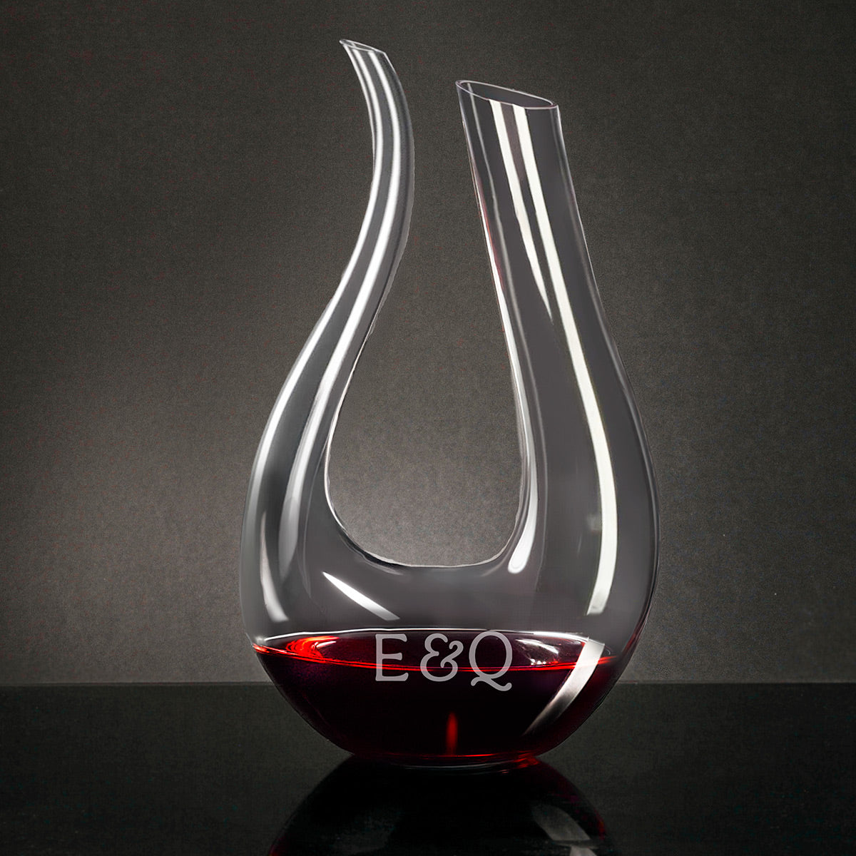 Curved glass wine decanter with red wine at the bottom, on a dark surface against a gray background.