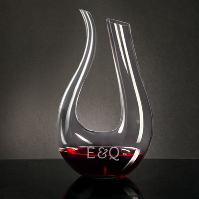 Curved glass wine decanter with red wine at the bottom, on a dark surface against a gray background.