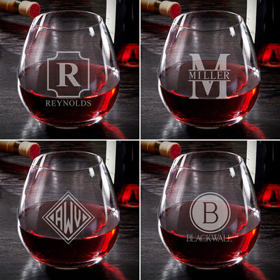 Four wine glasses with red wine, each etched with a different monogram, with wine bottles in the background.