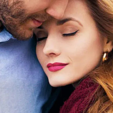 Close-up of a couple embracing, woman with closed eyes and pink lipstick resting against a man's chest.