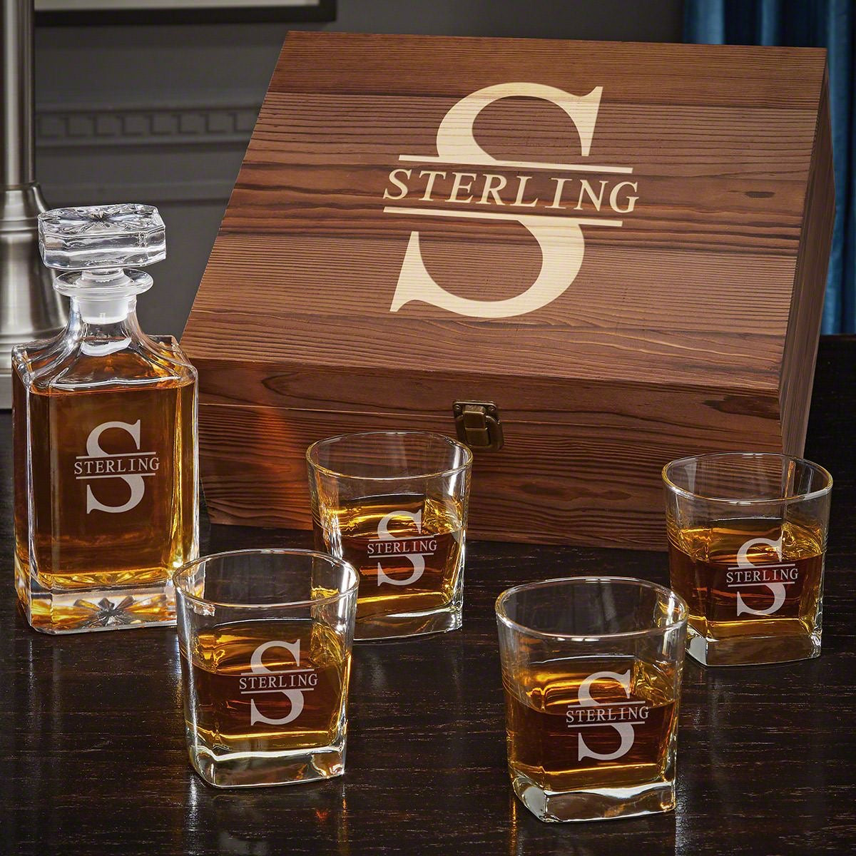 Wooden box labeled “S Sterling” with decanter and four whiskey glasses filled with amber liquid on a table.