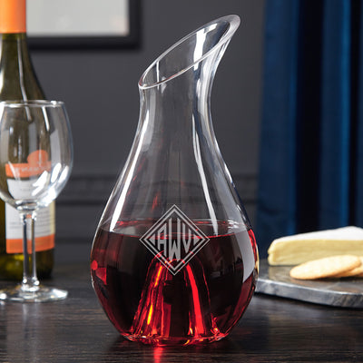 Glass wine decanter with red wine and “AWD” monogram; wine bottle, empty glass, and cheese on board in background