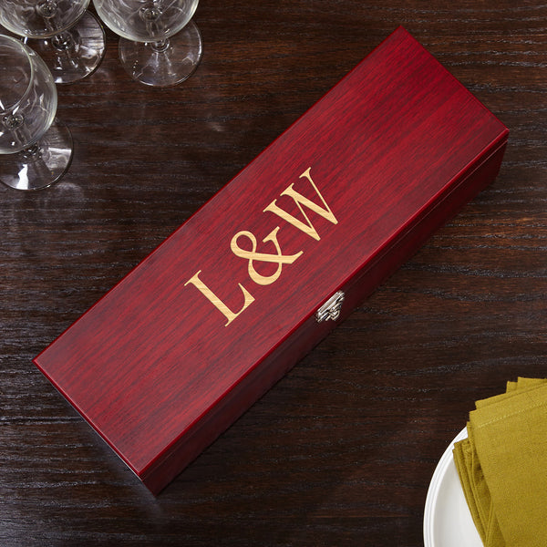Red wooden wine box with gold “L&W” lettering on a dark table, with wine glasses and folded napkins nearby.