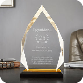 Glass award plaque with ExxonMobil and “25 years” text on a desk beside books and a leather chair.