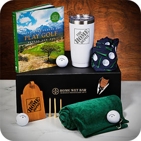 Golf gift set with book, tumbler, golf balls, tees, towel, divot tool, and small bag on a table.