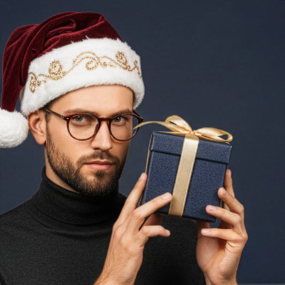 Man wearing Santa hat and glasses holding a navy gift box with gold ribbon against a dark background