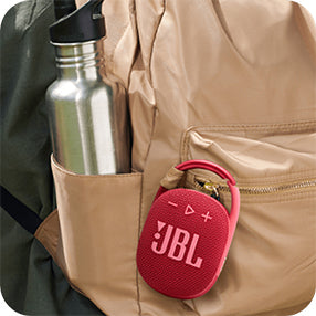 Red JBL clip-on speaker attached to beige backpack pocket next to a metal water bottle