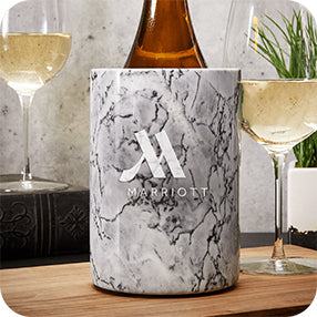Marble-patterned wine bottle chiller with Marriott logo, with wine glasses and greenery in the background