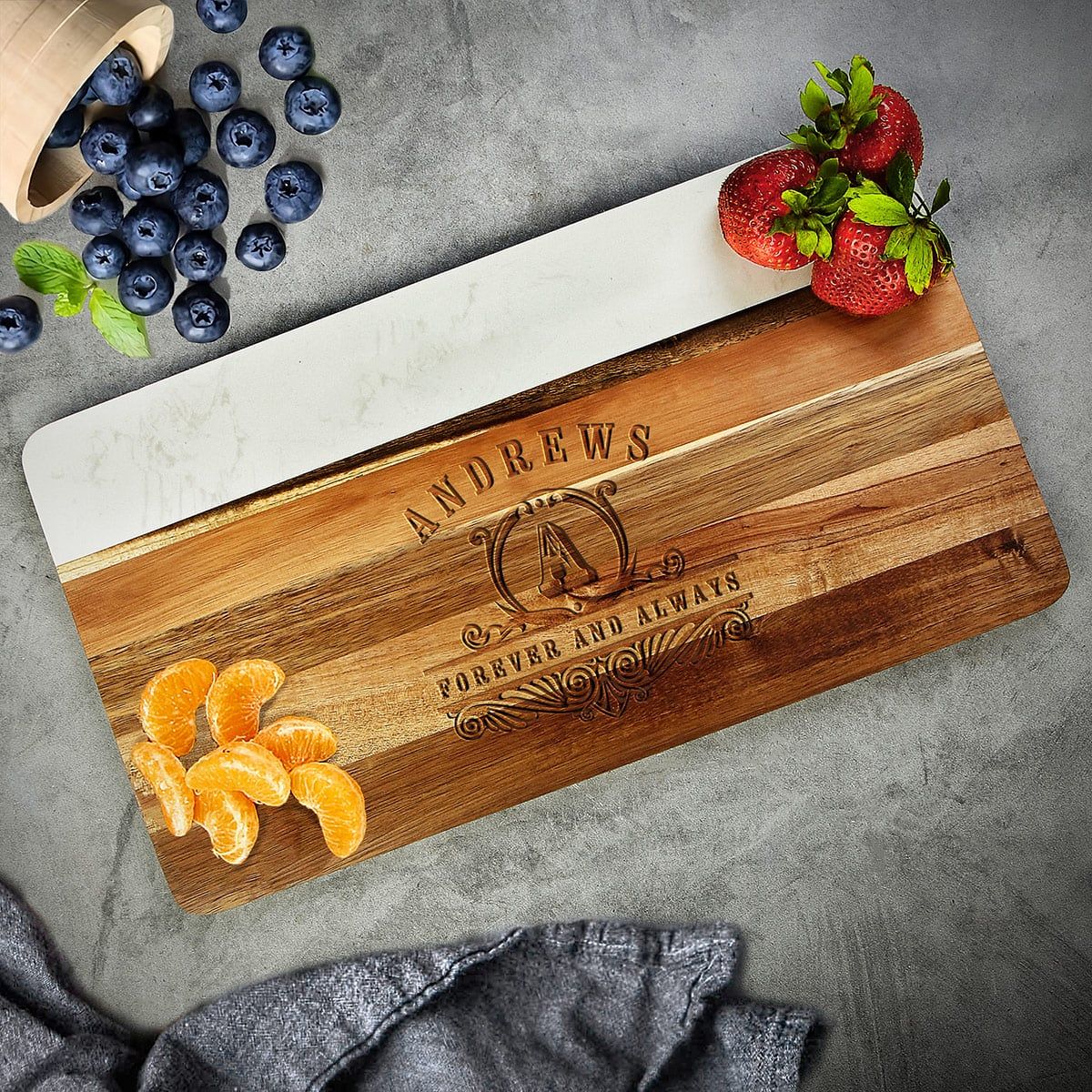 Wood and marble cutting board engraved “ANDREWS” and “FOREVER AND ALWAYS,” with strawberries, blueberries, and orange slices.